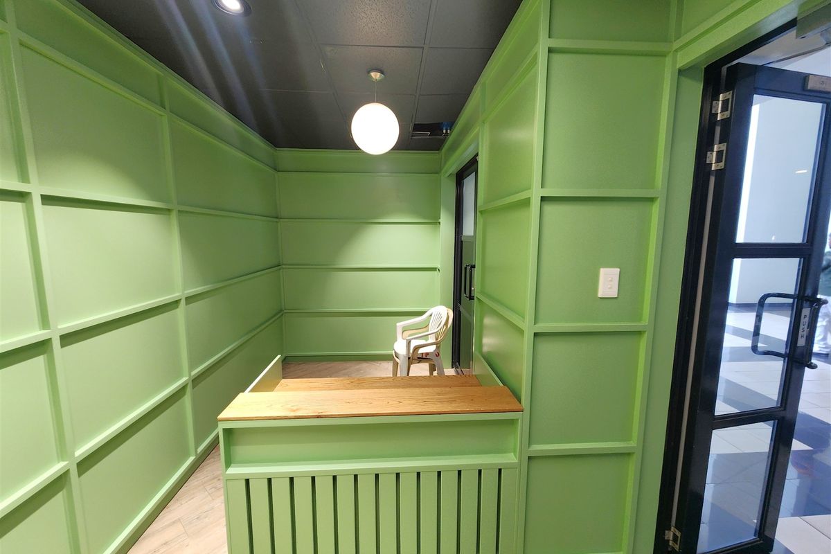 A compact office space featuring vibrant green wainscoting, a built-in reception desk, and modern lighting fixtures.