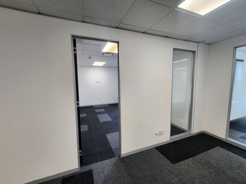A vacant office space featuring a suspended ceiling, recessed lighting, carpet tiles, and glass partitions, offering a clean and professional work environment.