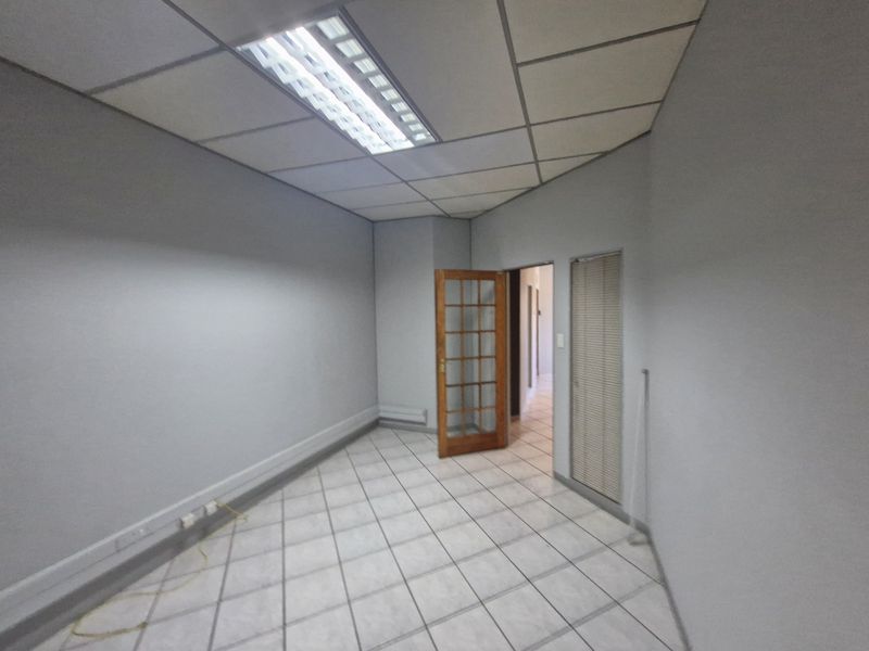An empty commercial office space featuring tiled flooring, a suspended ceiling with integrated lighting, and a timber-framed glass door.