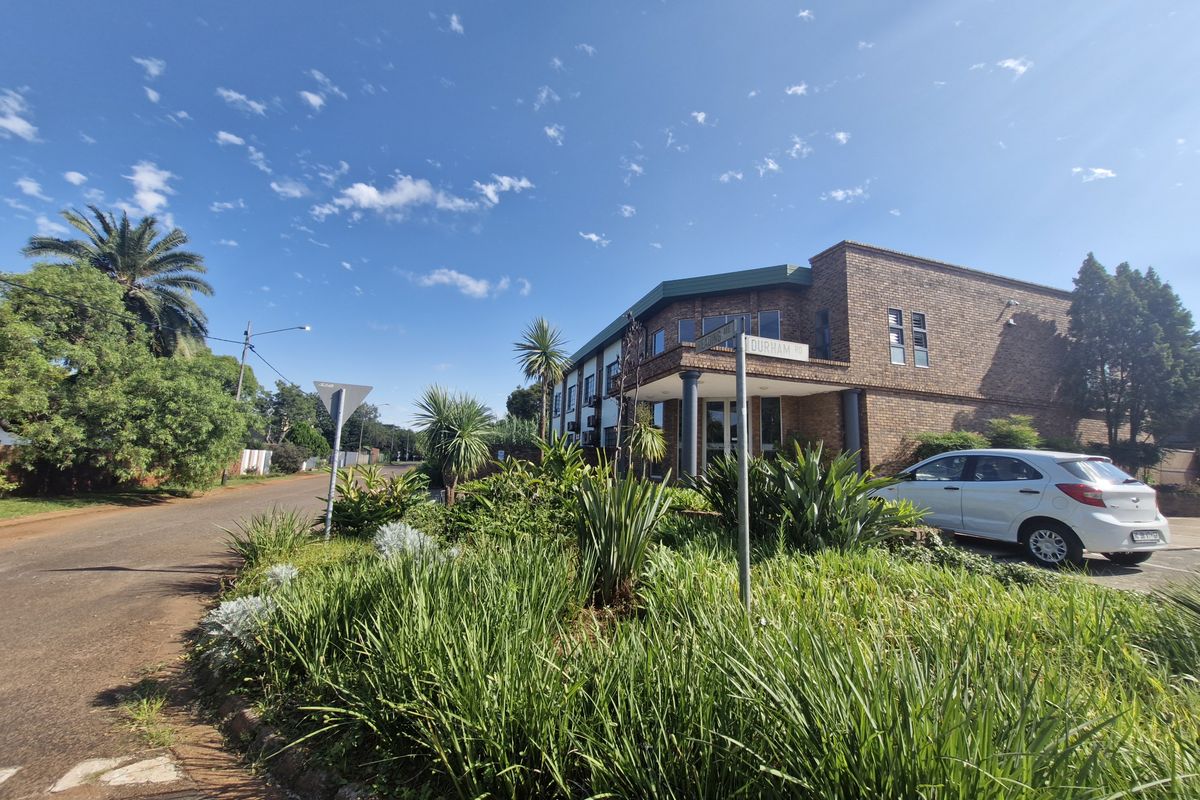 A street-level view of a commercial brick building featuring a landscaped garden, paved driveway, and a covered entrance area.