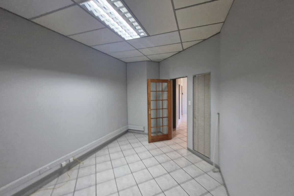 An empty commercial office space featuring tiled flooring, a suspended ceiling with integrated lighting, and a timber-framed glass door.