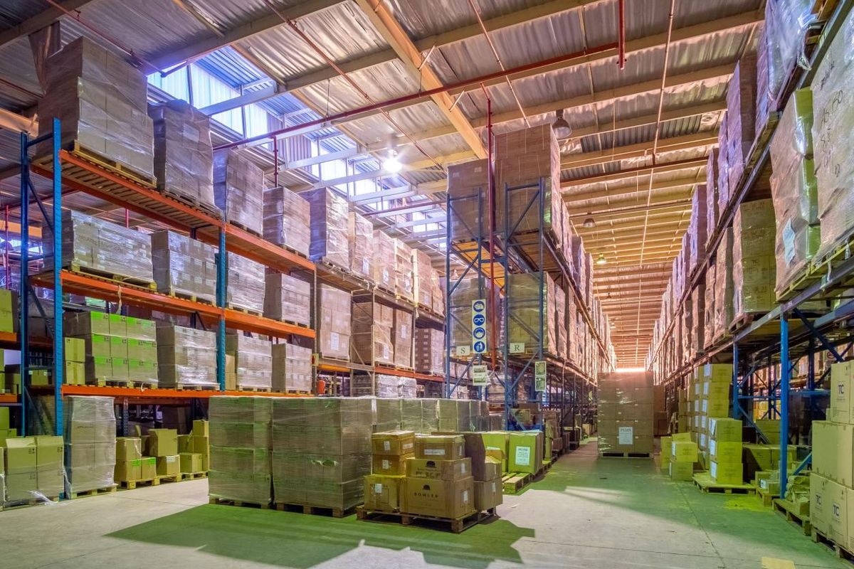 Spacious industrial warehouse featuring high-clearance steel racking systems, exposed roof structure with integrated skylights, and durable concrete flooring.