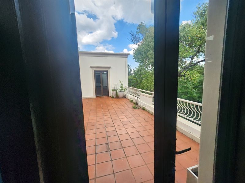Spacious outdoor balcony featuring terracotta tiling and a decorative wrought iron balustrade, offering an open-air space accessible from the office interior.