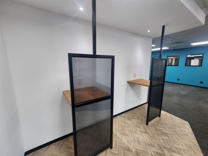 Modern office space featuring built-in workstations with metal and glass privacy screens, recessed lighting, and a combination of herringbone and carpeted flooring.