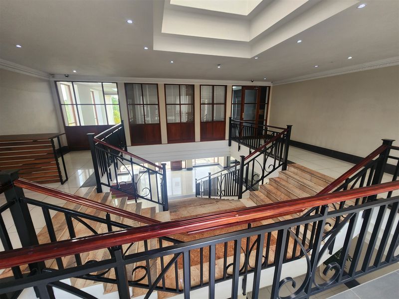 Spacious office building hallway featuring a grand central staircase with wrought iron balustrades, wooden handrails, and a large overhead skylight.