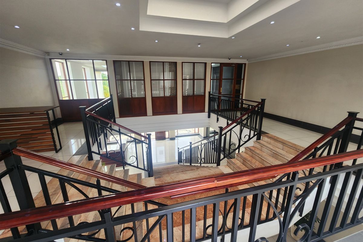 Spacious office building hallway featuring a grand central staircase with wrought iron balustrades, wooden handrails, and a large overhead skylight.