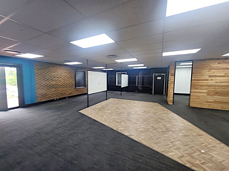 Spacious open-plan office area featuring a mix of carpet and parquet flooring, wood-paneled walls, and recessed ceiling lighting.