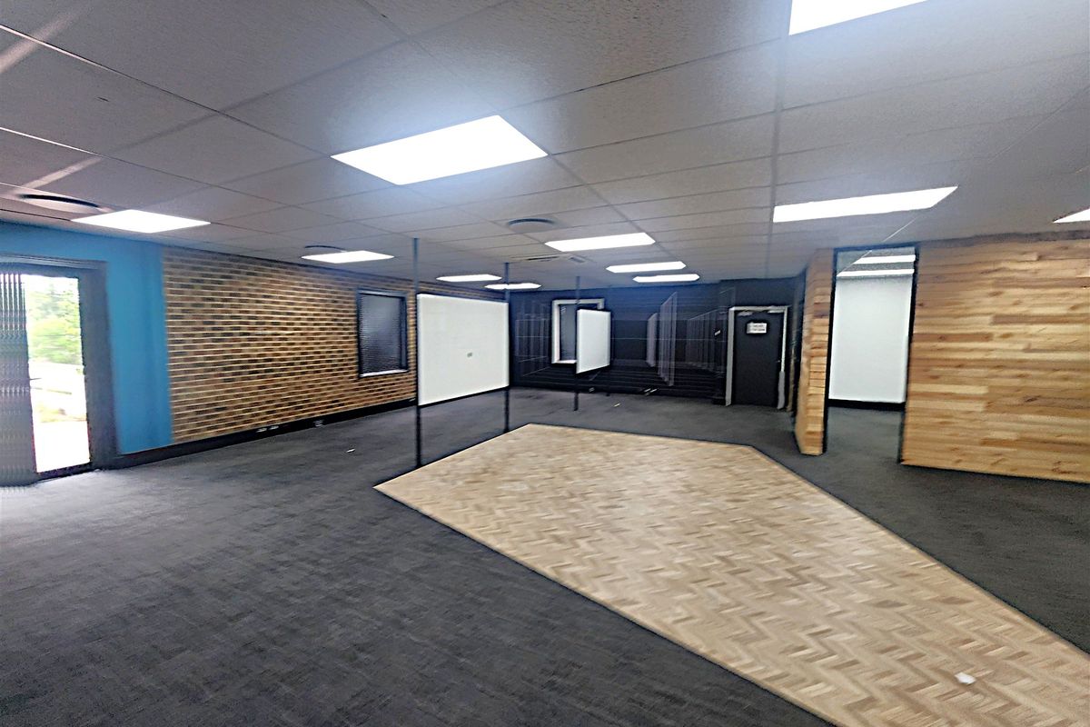 Spacious open-plan office area featuring a mix of carpet and parquet flooring, wood-paneled walls, and recessed ceiling lighting.