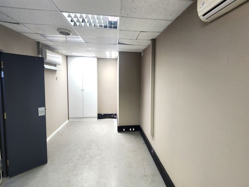 An empty office space featuring a suspended ceiling, dual split-system air conditioning units, and a built-in storage cupboard.