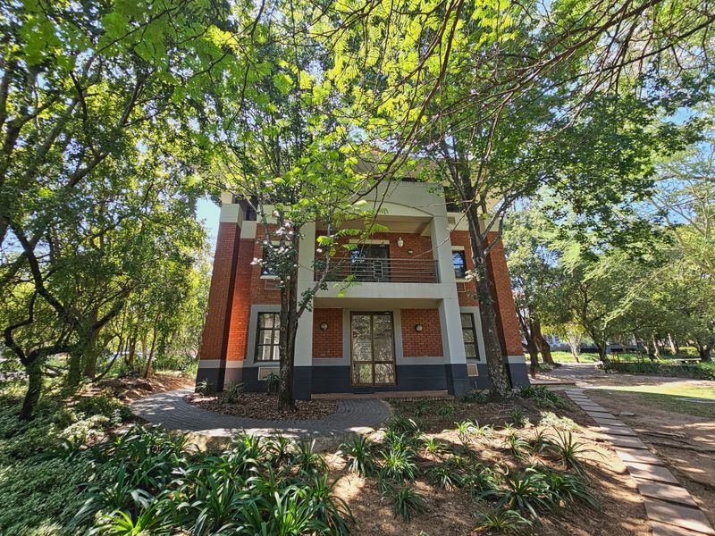 A well-maintained multi-story office building featuring a red brick facade, a private balcony, and a landscaped garden setting with mature trees.