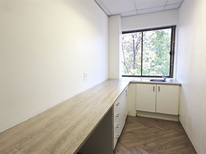 A clean, functional utility or kitchenette area featuring modern laminate countertops, built-in cabinetry, a stainless steel sink, and durable herringbone vinyl flooring.