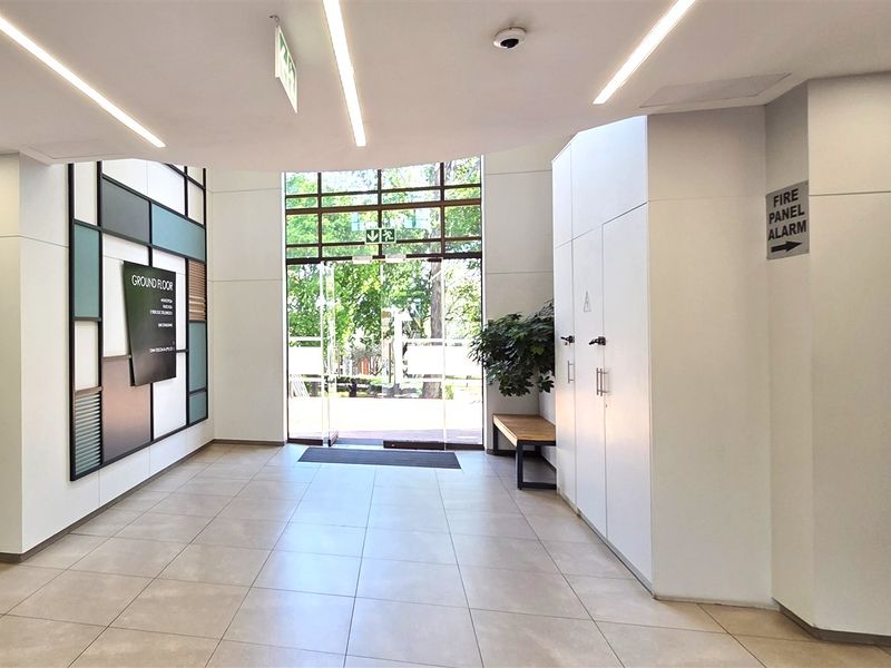 Modern office building entrance lobby featuring clean white finishes, recessed linear lighting, tiled flooring, and integrated directional signage.
