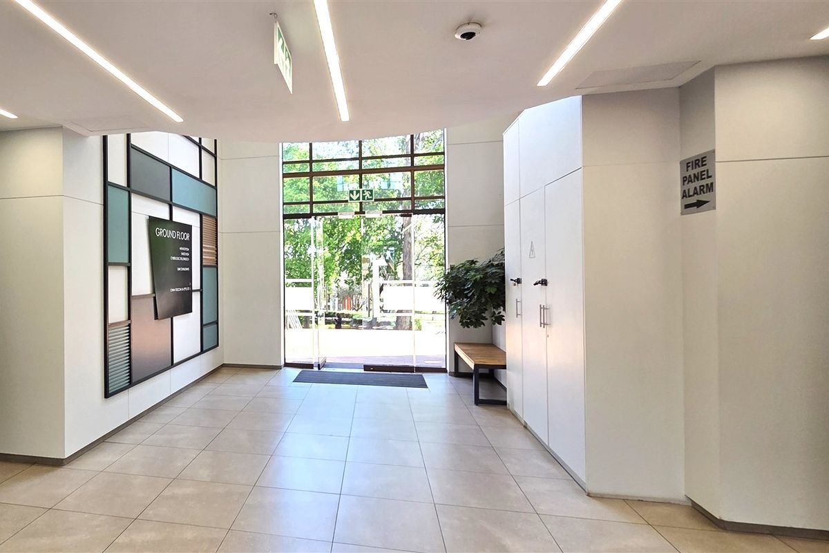 Modern office building entrance lobby featuring clean white finishes, recessed linear lighting, tiled flooring, and integrated directional signage.