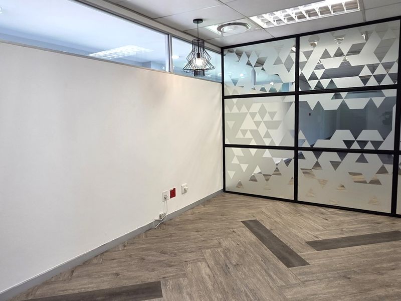 A modern, empty office space featuring contemporary herringbone flooring, a decorative glass partition wall, and professional recessed lighting.