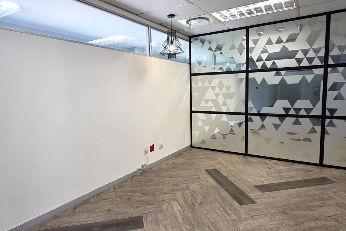 A modern, empty office space featuring contemporary herringbone flooring, a decorative glass partition wall, and professional recessed lighting.