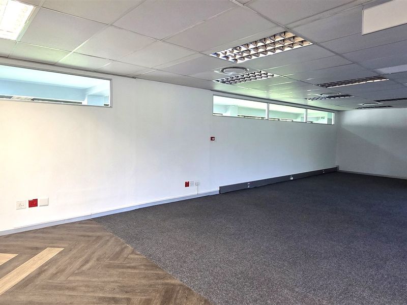 A spacious, vacant office area featuring a mix of herringbone vinyl and carpet flooring, suspended ceilings, and clerestory windows for natural light.