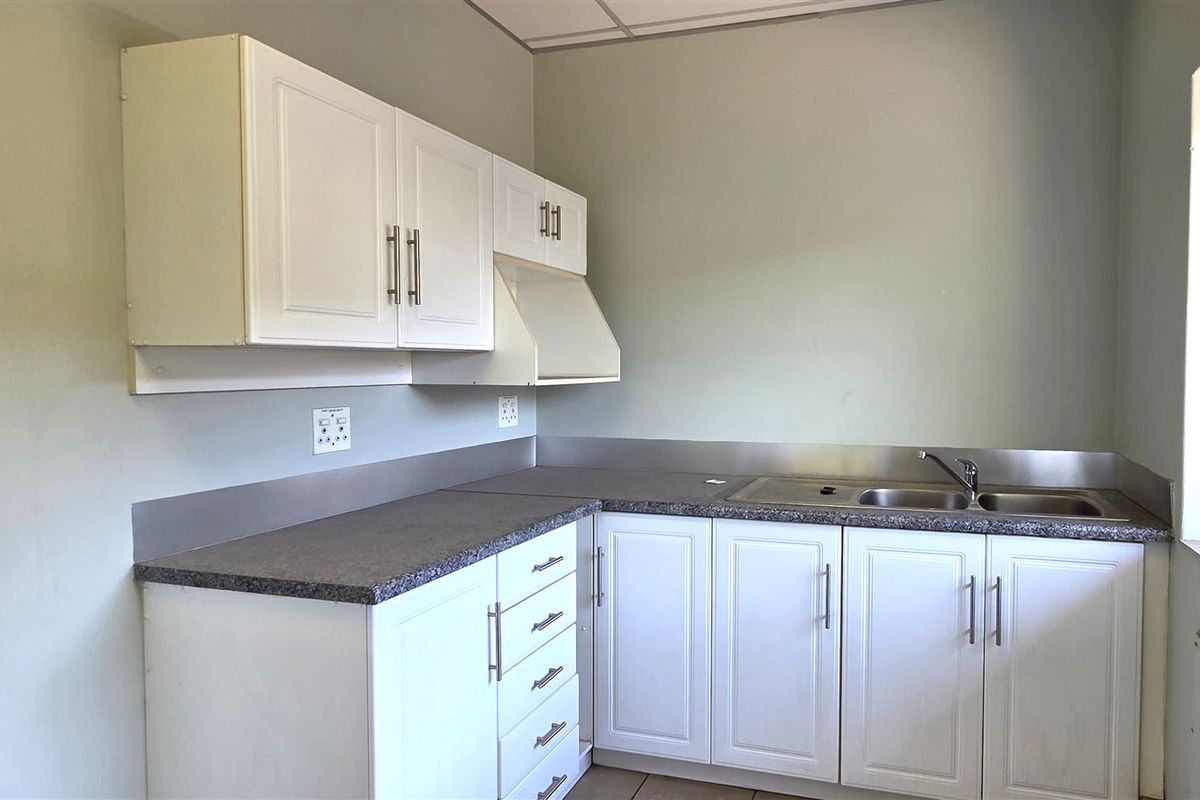A functional office kitchenette featuring white cabinetry, laminate countertops, a stainless steel sink, and a stainless steel splashback.