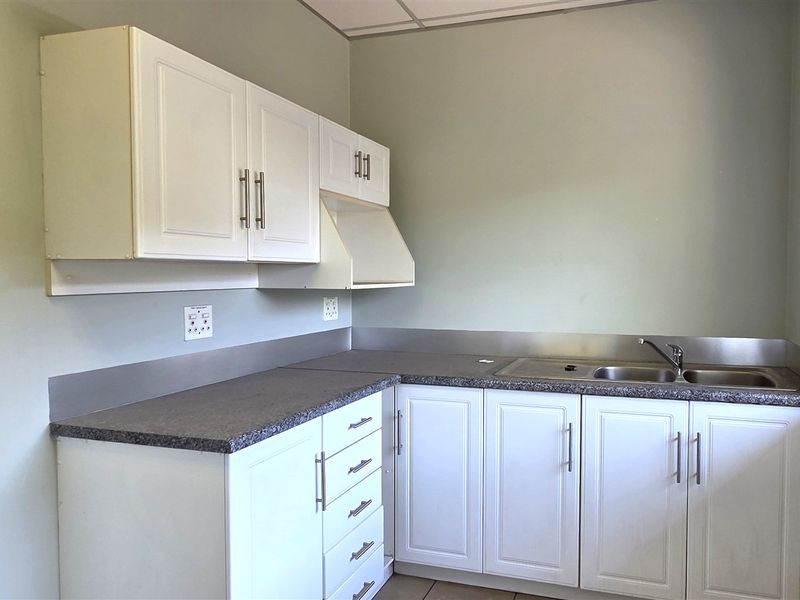 A functional office kitchenette featuring white cabinetry, laminate countertops, a stainless steel sink, and a stainless steel splashback.
