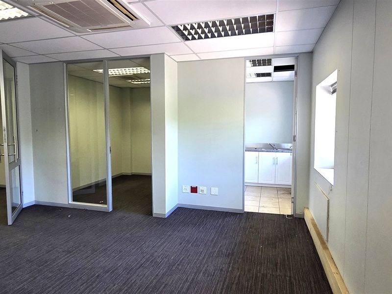 Empty office space featuring glass partitions, carpeted flooring, recessed lighting, and a small integrated kitchenette area.
