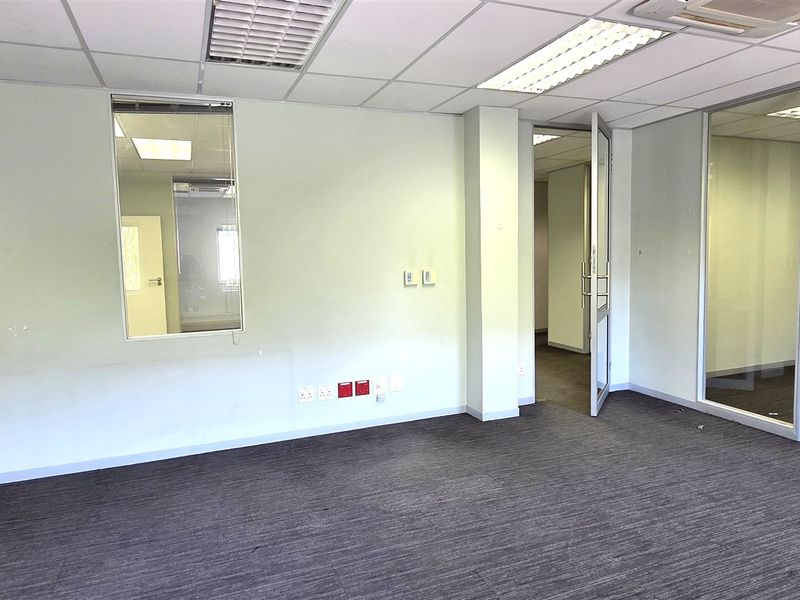 A clean, vacant office space featuring carpeted flooring, a suspended ceiling with recessed lighting, and a glass partition wall for a modern, professional layout.