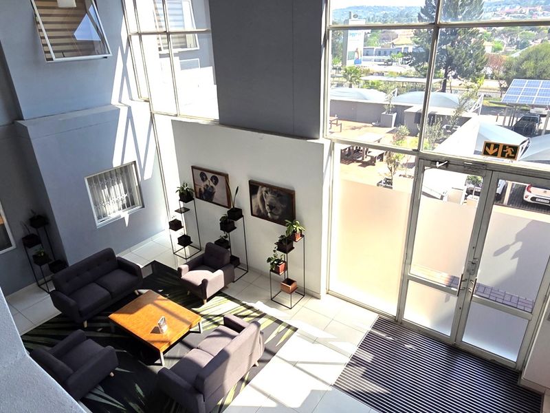 Bright and spacious double-volume office entrance lobby featuring large glass windows, modern tiled flooring, and direct access to the exterior parking area.