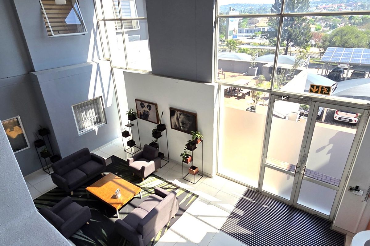 Bright and spacious double-volume office entrance lobby featuring large glass windows, modern tiled flooring, and direct access to the exterior parking area.