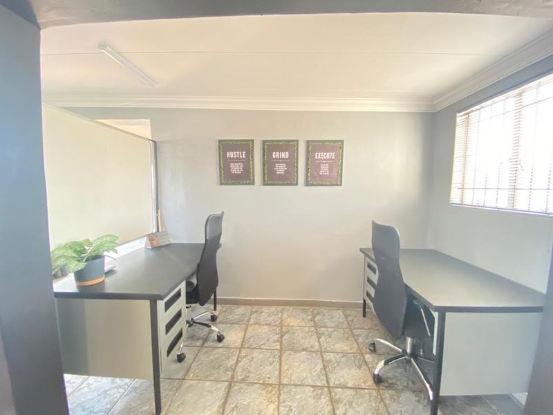 A functional office space featuring tiled flooring, natural light through venetian blinds, and overhead fluorescent lighting, suitable for a professional work environment.