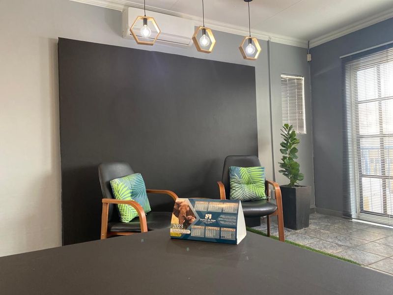 A modern office space featuring dark accent wall, split-system air conditioning, pendant lighting, and tiled flooring with natural light from large windows.