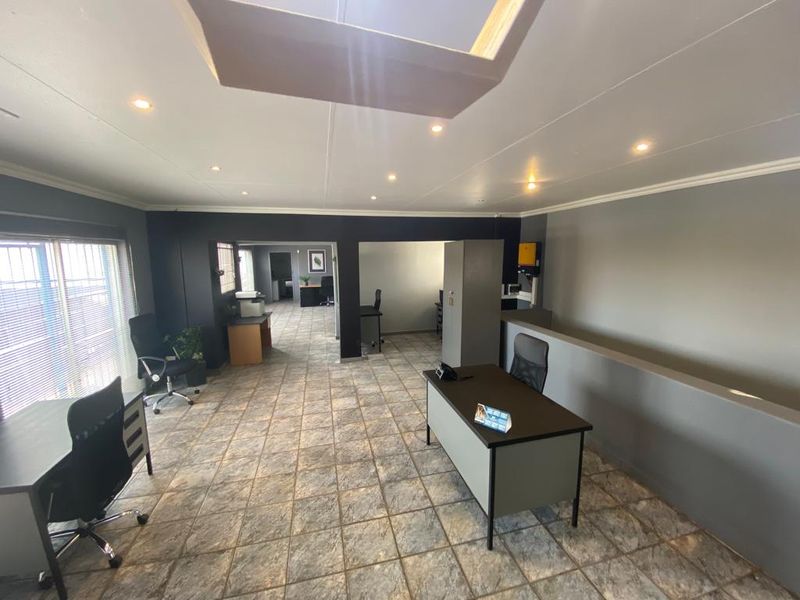 Open-plan commercial office space featuring tiled flooring, recessed lighting, and partitioned work areas with security-fitted windows.