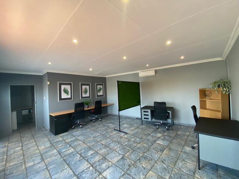 A functional commercial office space featuring tiled flooring, recessed downlighting, a wall-mounted air conditioning unit, and a built-in desk configuration.