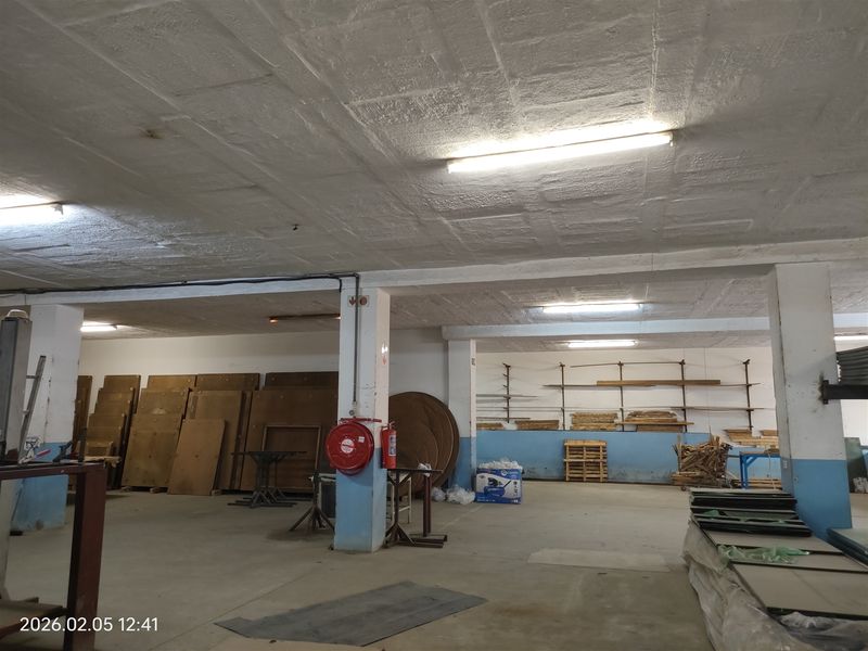 Spacious industrial utility area featuring concrete flooring, exposed ceiling, wall-mounted shelving, and essential fire safety equipment.