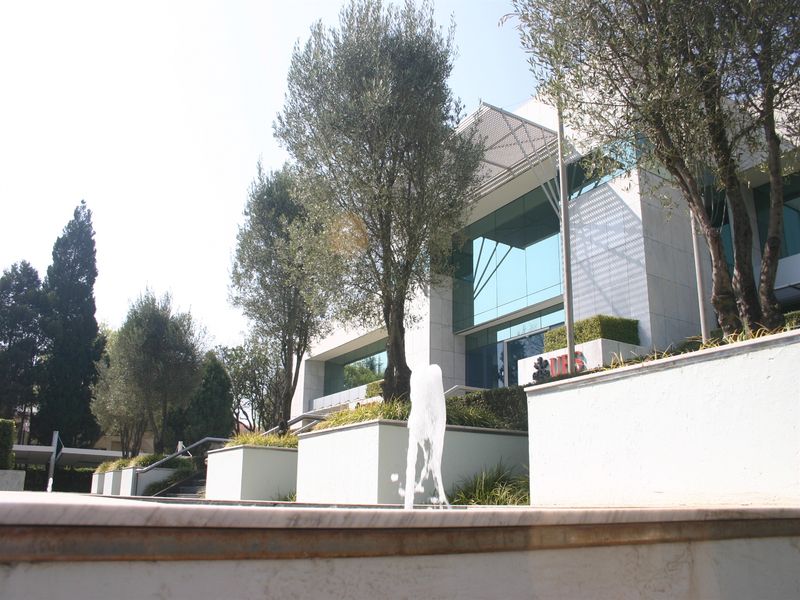 Modern office building exterior featuring a glass facade, stone cladding, and a prominent water feature set within a landscaped garden.