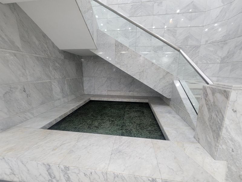 A modern office entrance featuring high-end marble wall and floor finishes, a glass balustrade staircase, and a built-in decorative water feature.