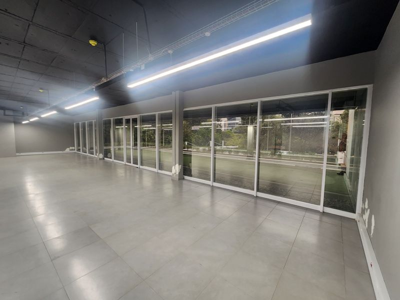 Spacious open-plan office area featuring an exposed ceiling, modern linear lighting, and extensive glass sliding doors providing natural light and outdoor access.