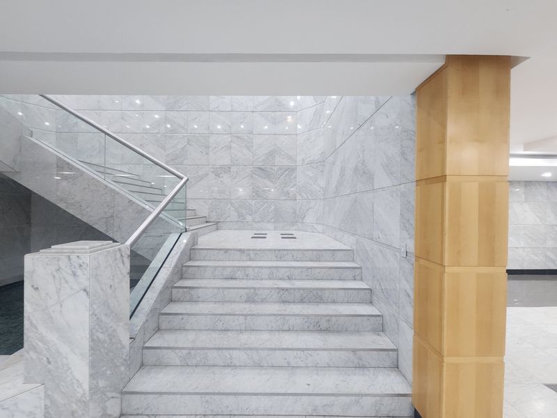 Elegant office building entrance featuring a grand marble staircase with glass balustrades and high-quality marble wall finishes.