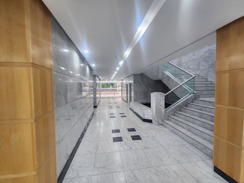 A spacious, modern office building lobby featuring high-end marble flooring, marble wall finishes, and a prominent stone staircase with a glass balustrade.
