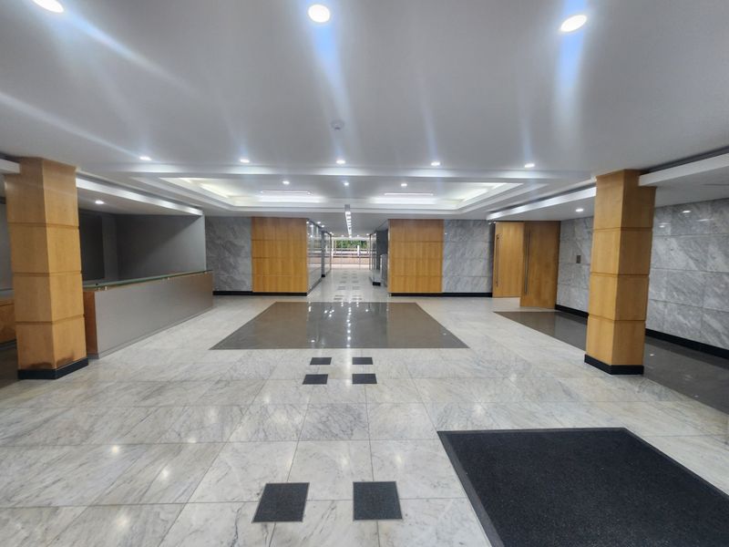 Spacious office building lobby featuring polished marble flooring, recessed ceiling lighting, and elegant wood and marble wall paneling.