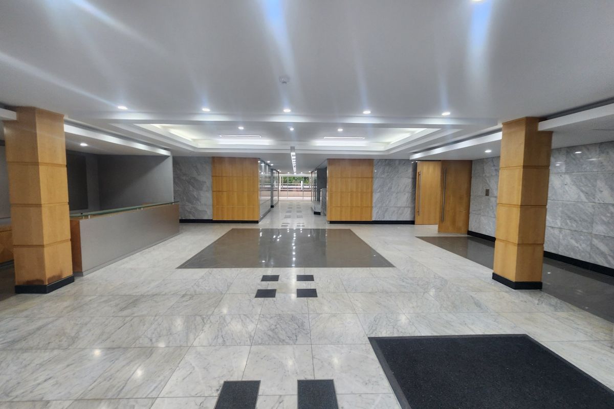 Spacious office building lobby featuring polished marble flooring, recessed ceiling lighting, and elegant wood and marble wall paneling.