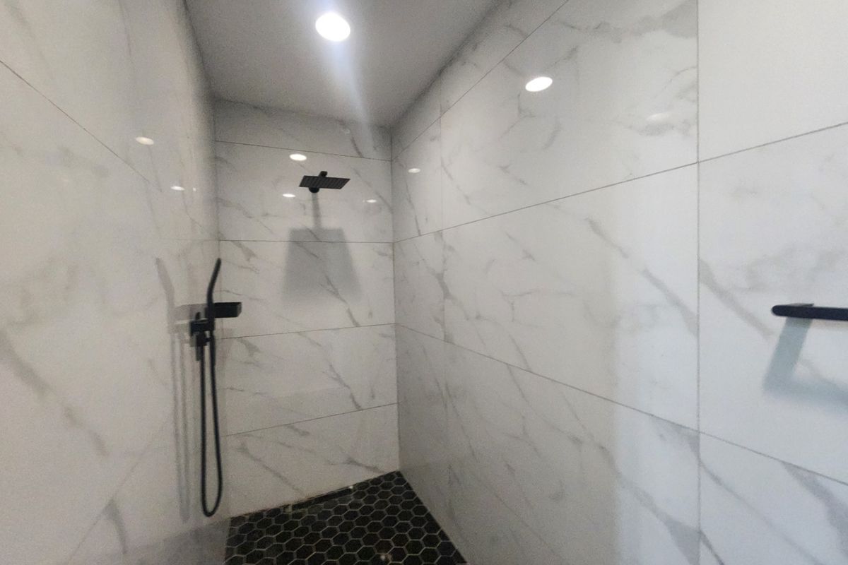 Modern walk-in shower featuring marble-look wall tiles, contrasting black hexagonal floor tiles, and contemporary matte black shower fixtures.