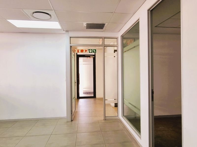 A bright, vacant office space featuring tiled flooring, suspended ceilings with recessed lighting, and modern glass partition walls creating a professional, open work environment.