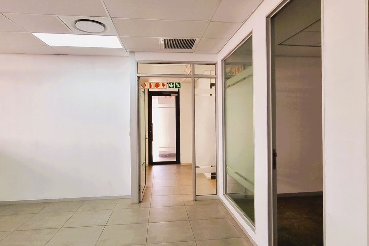 A bright, vacant office space featuring tiled flooring, suspended ceilings with recessed lighting, and modern glass partition walls creating a professional, open work environment.