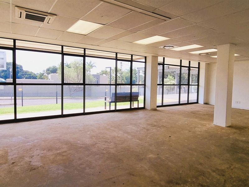 Spacious, empty open-plan office area featuring large floor-to-ceiling windows, suspended ceilings with recessed lighting, and central air conditioning.
