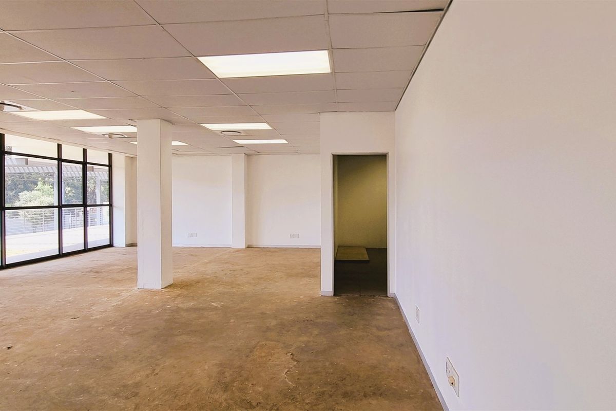 A spacious, vacant open-plan office area featuring large windows, suspended ceilings with recessed lighting, and concrete flooring, offering a blank canvas for customization.