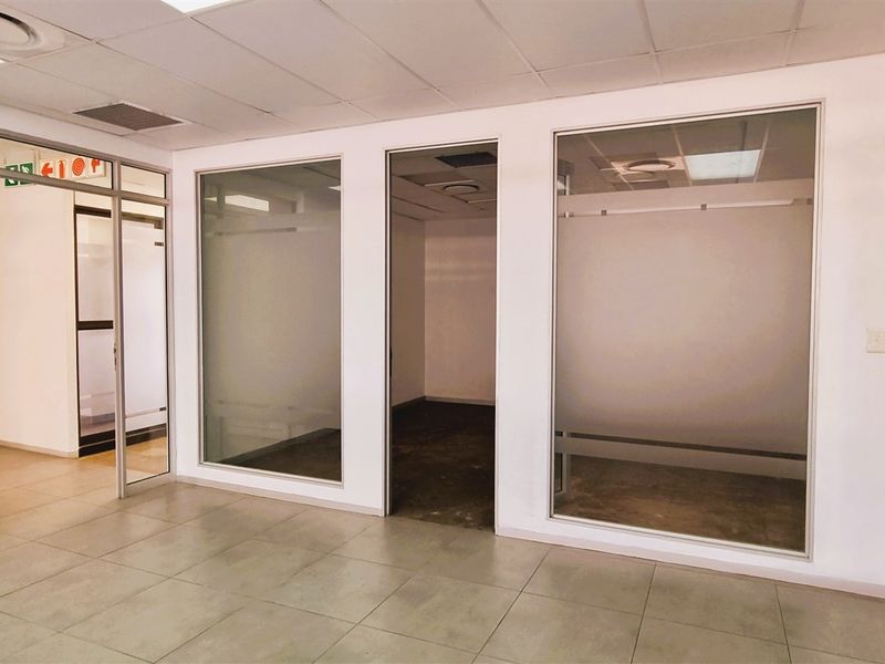 A bright, vacant office space featuring modern glass partitioning, tiled flooring, and a suspended ceiling with integrated lighting.