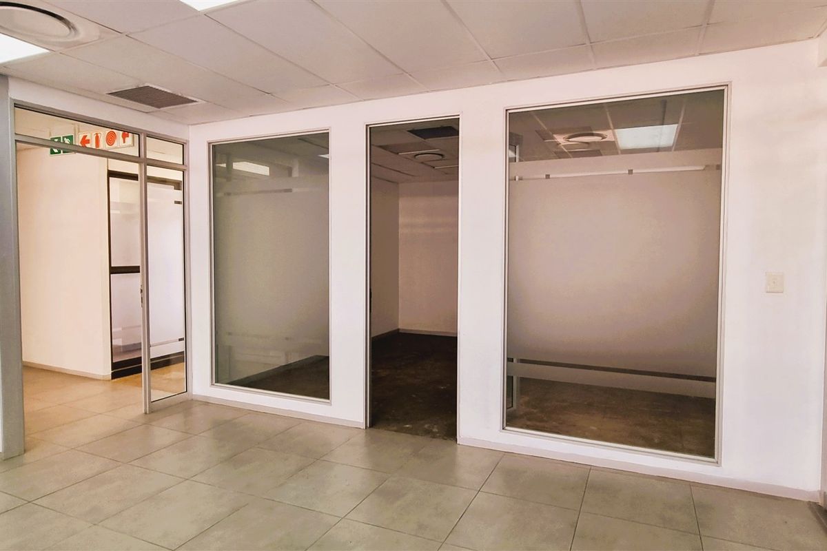 A bright, vacant office space featuring modern glass partitioning, tiled flooring, and a suspended ceiling with integrated lighting.