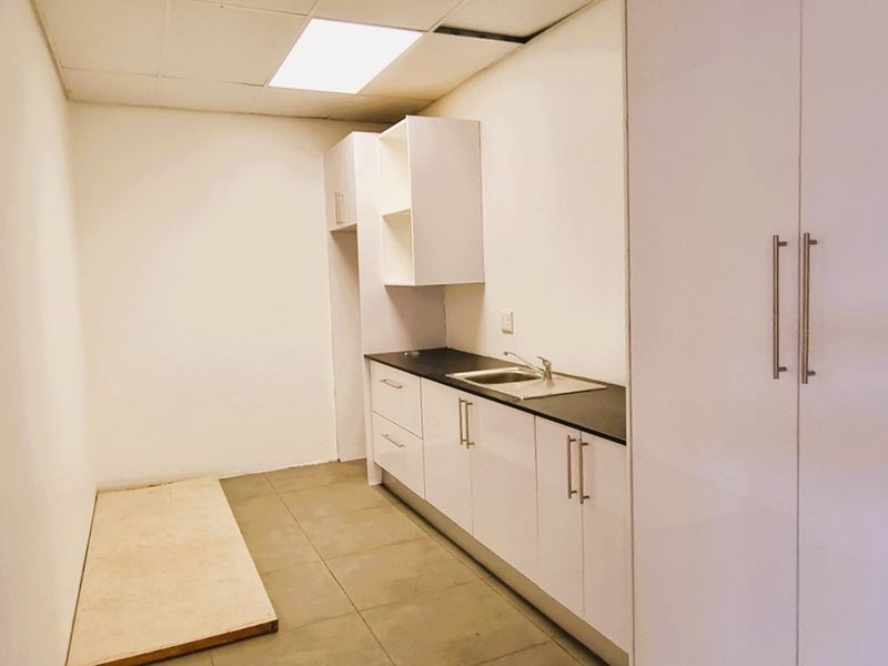A compact office kitchenette featuring white built-in cabinetry, a sink, tiled flooring, and a drop ceiling with recessed lighting.