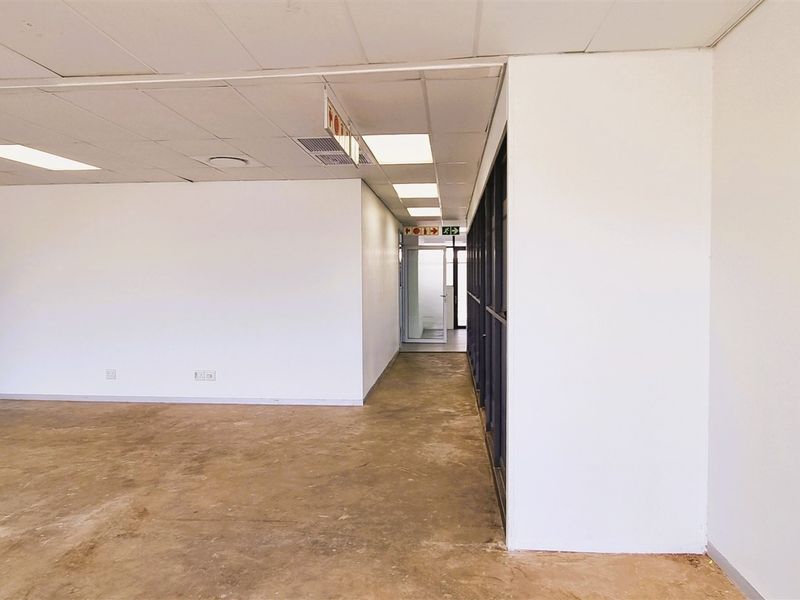 An open-plan office space featuring a suspended ceiling, recessed lighting, and internal glass partitioning, currently vacant with unfinished concrete flooring.