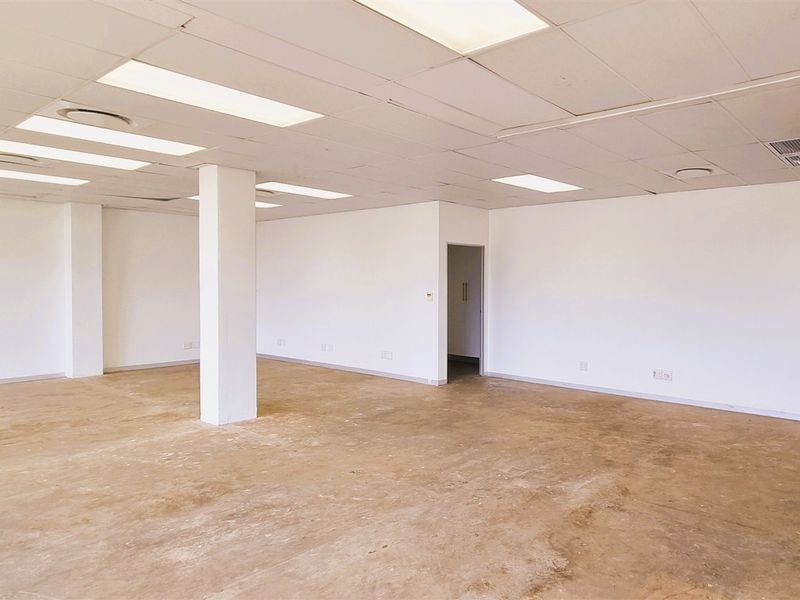 An open-plan office space featuring a suspended ceiling with recessed lighting, a structural column, and unfinished concrete flooring.