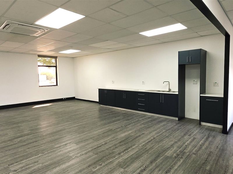 A spacious, modern office area featuring a built-in kitchenette, suspended ceiling with recessed lighting, cassette air conditioning, and durable laminate flooring.