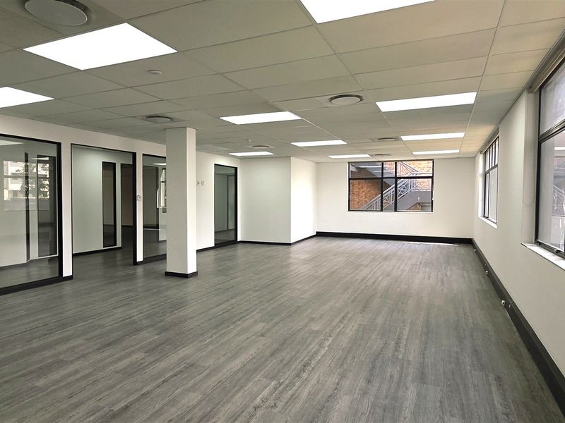 A bright, open-plan office space featuring modern laminate flooring, glass partitions, and recessed ceiling lighting, offering a clean and professional work environment.